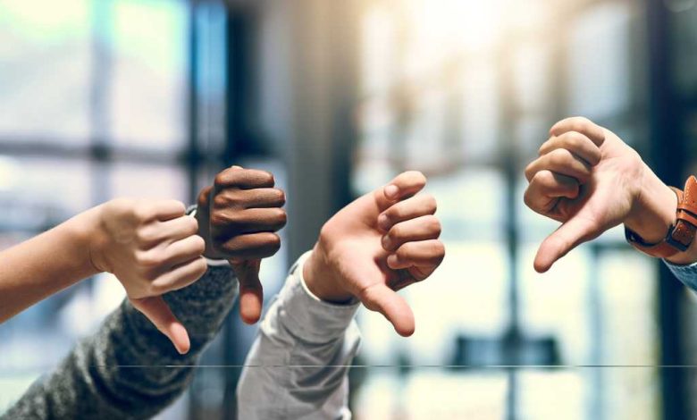 four hands raised with thumbs down in front of window with blurred light