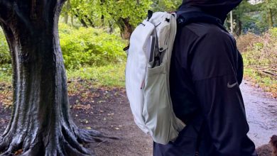 The Outdoor Backpack worn outside in profile next to a damp tree with lots of green foliage in the background.