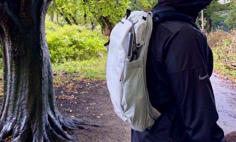 The Outdoor Backpack worn outside in profile next to a damp tree with lots of green foliage in the background.