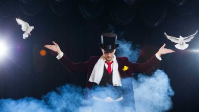 Magician with two flying white Doves on a black background shrouded in mysterious blue smoke