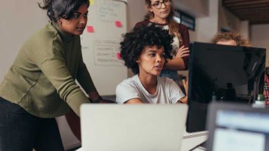 Software engineers working on project and programming in company. Startup business group working as team to find solution to problem. Woman programmer working on computer with colleagues standing by.