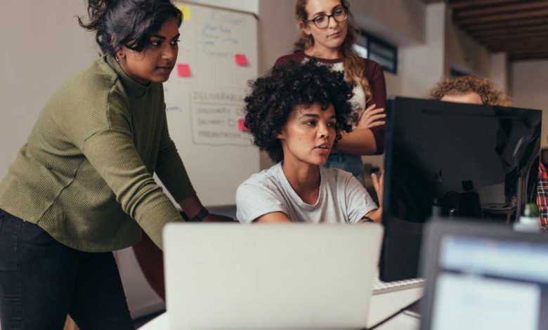 Software engineers working on project and programming in company. Startup business group working as team to find solution to problem. Woman programmer working on computer with colleagues standing by.