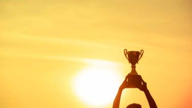 Winner holding golden trophy cup above head sun and golden sky in background