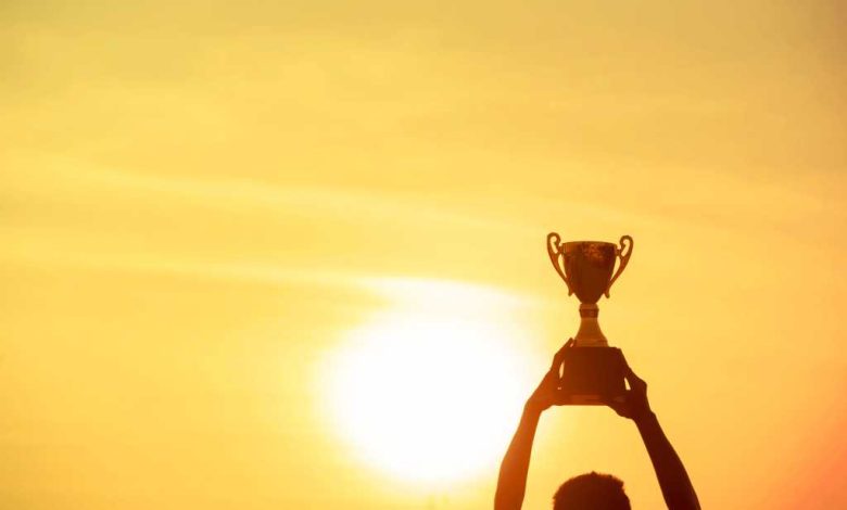 Winner holding golden trophy cup above head sun and golden sky in background